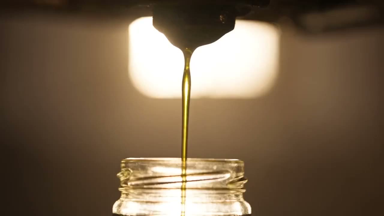 Frisch gepresstes Olivenöl läuft in goldenem Strahl aus der Steinpresse in ein Glas